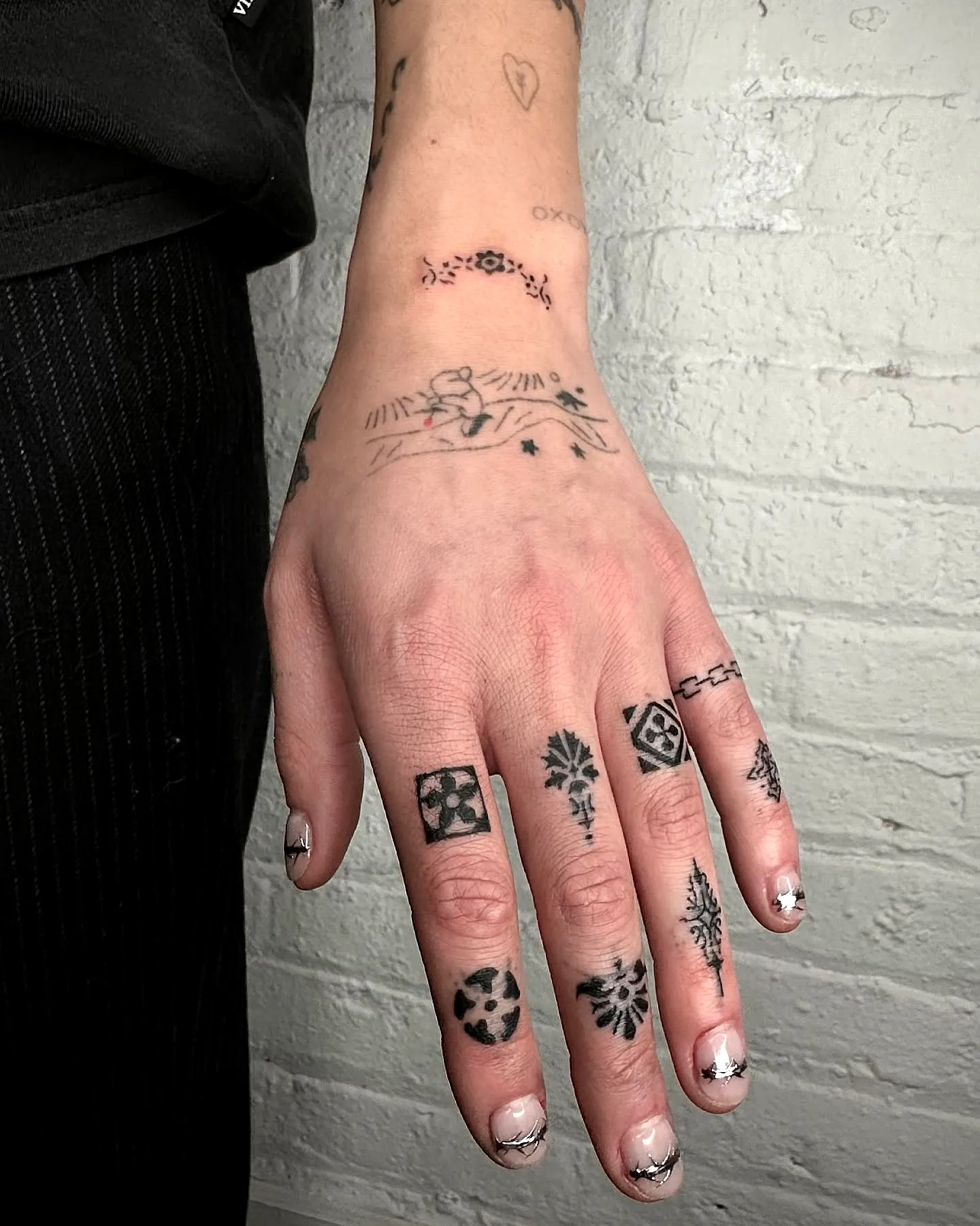 Dainty black finger tattoo for women with intricate floral and geometric designs