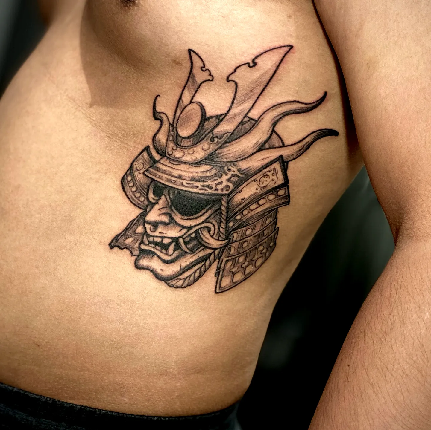 Detailed samurai mask torso tattoo in black ink
