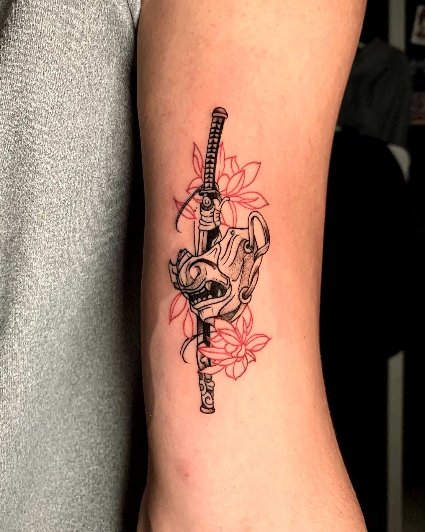 Hand holding sword with floral elements Samurai mask tattoo on arm