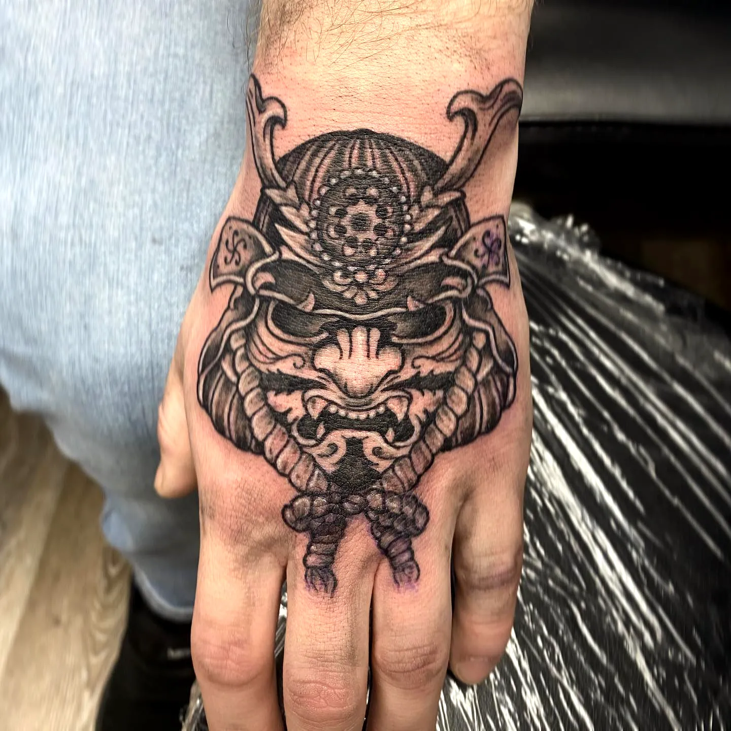 Intricate Samurai Mask Hand Tattoo in Bold Black Ink