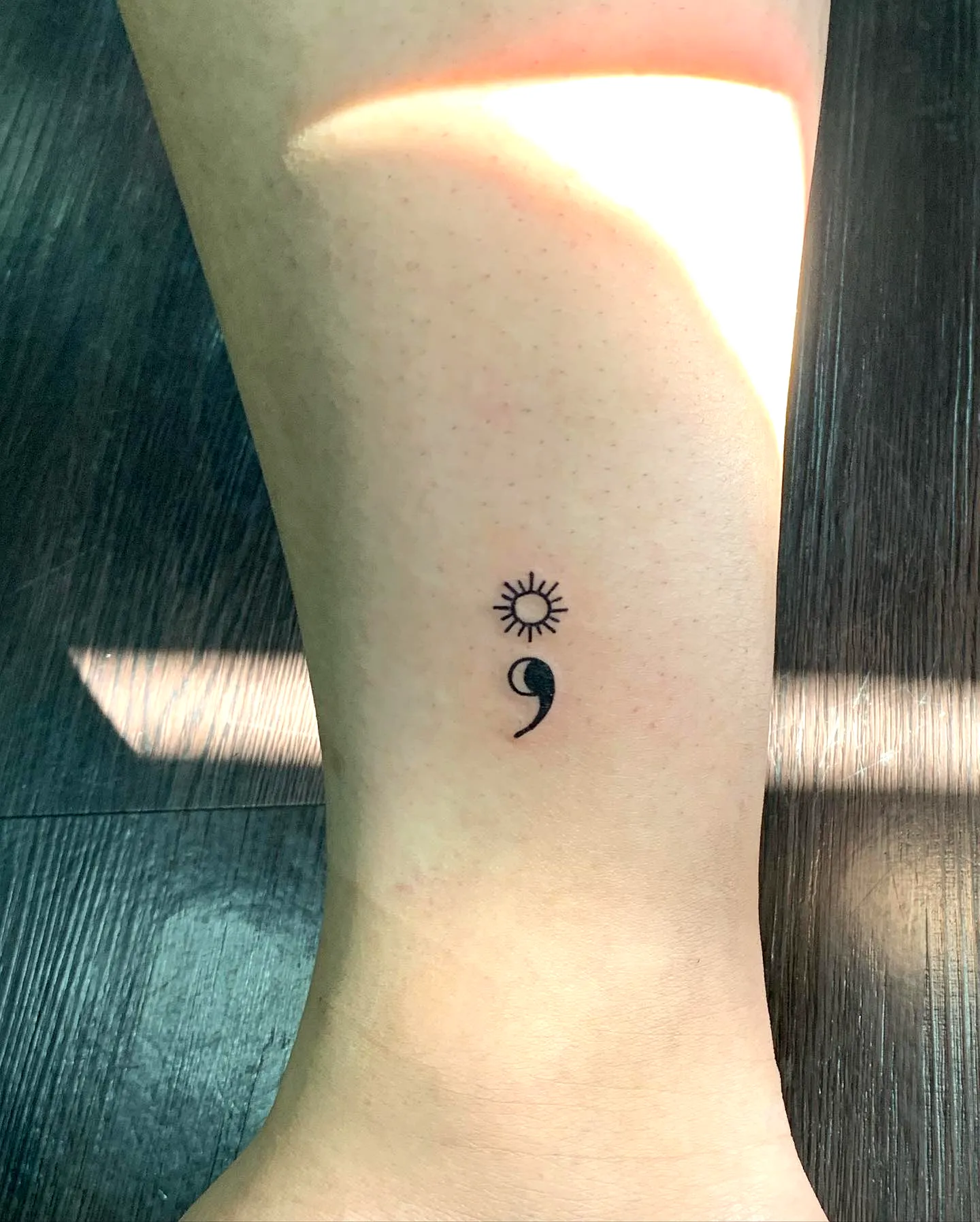 Minimalist sun and semicolon tattoo on lower leg