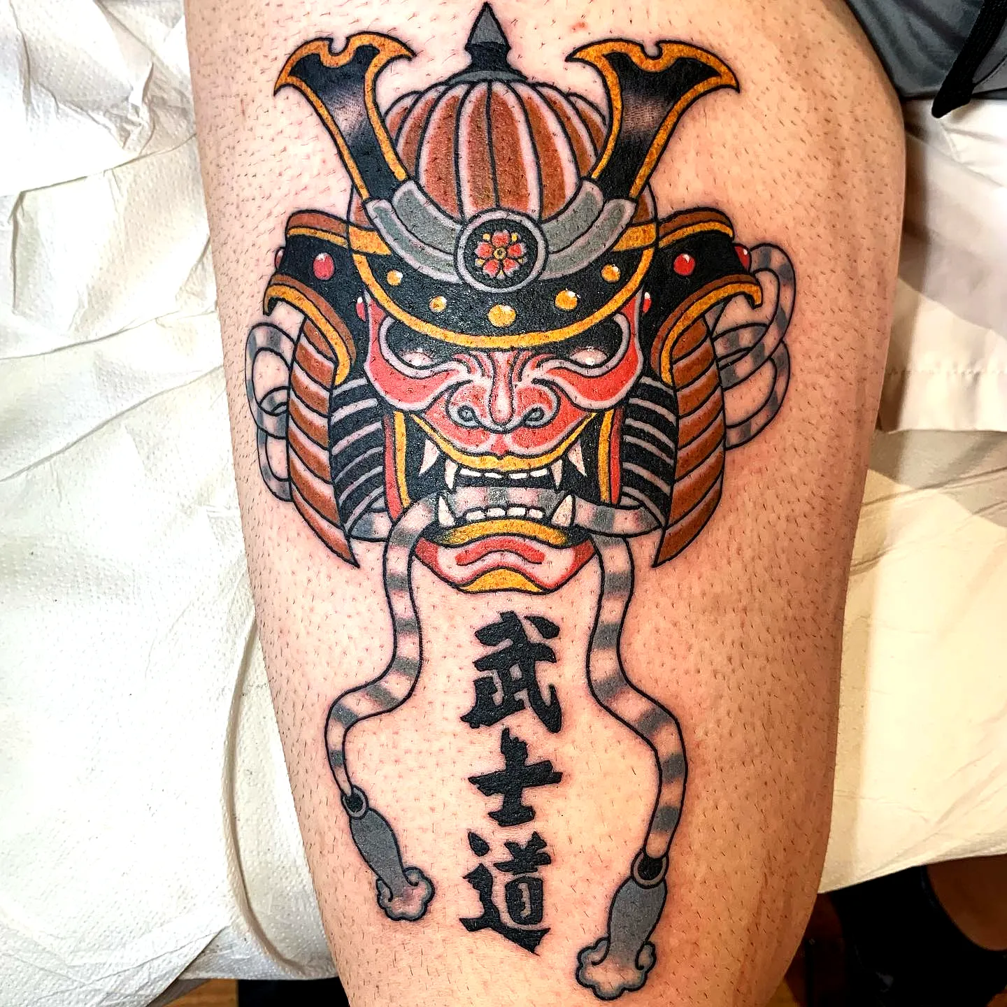 Samurai mask leg tattoo with bold red and orange details