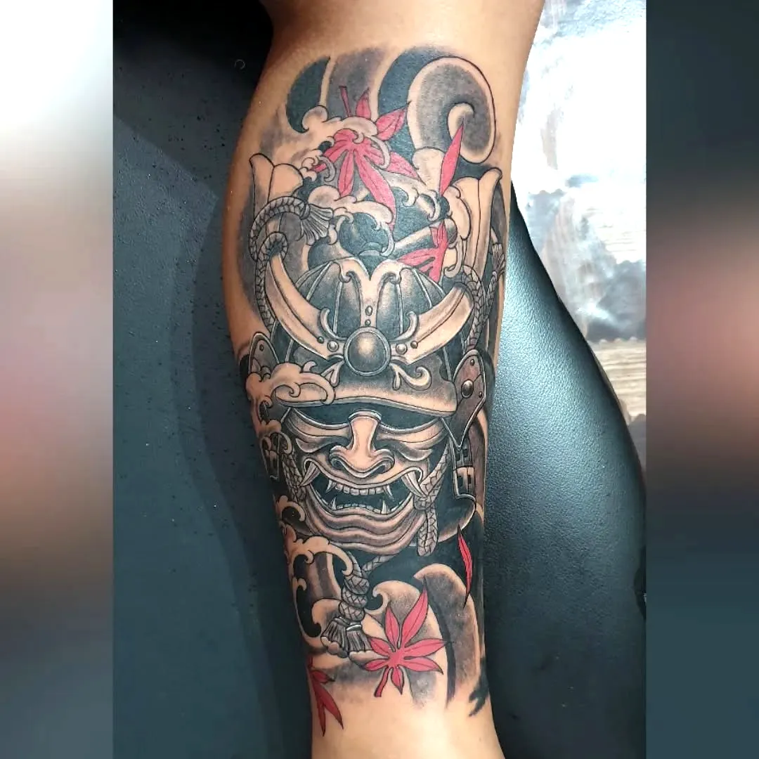 Samurai mask tattoo on lower leg with swirling clouds and red maple leaves