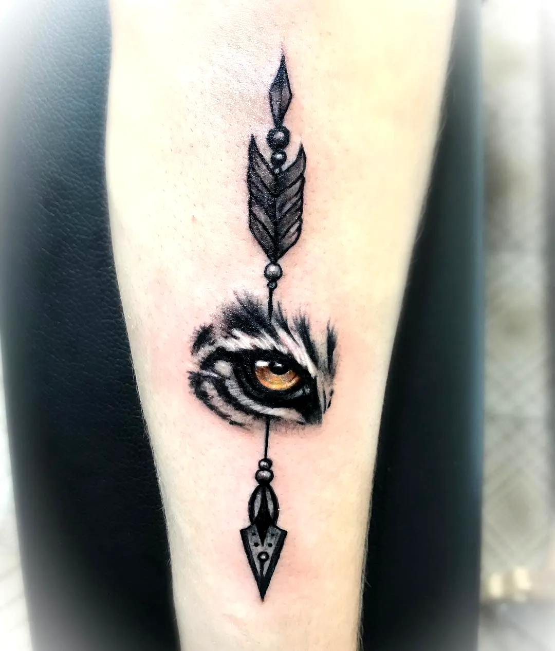 Stylized tiger eye tattoo with arrow design on forearm
