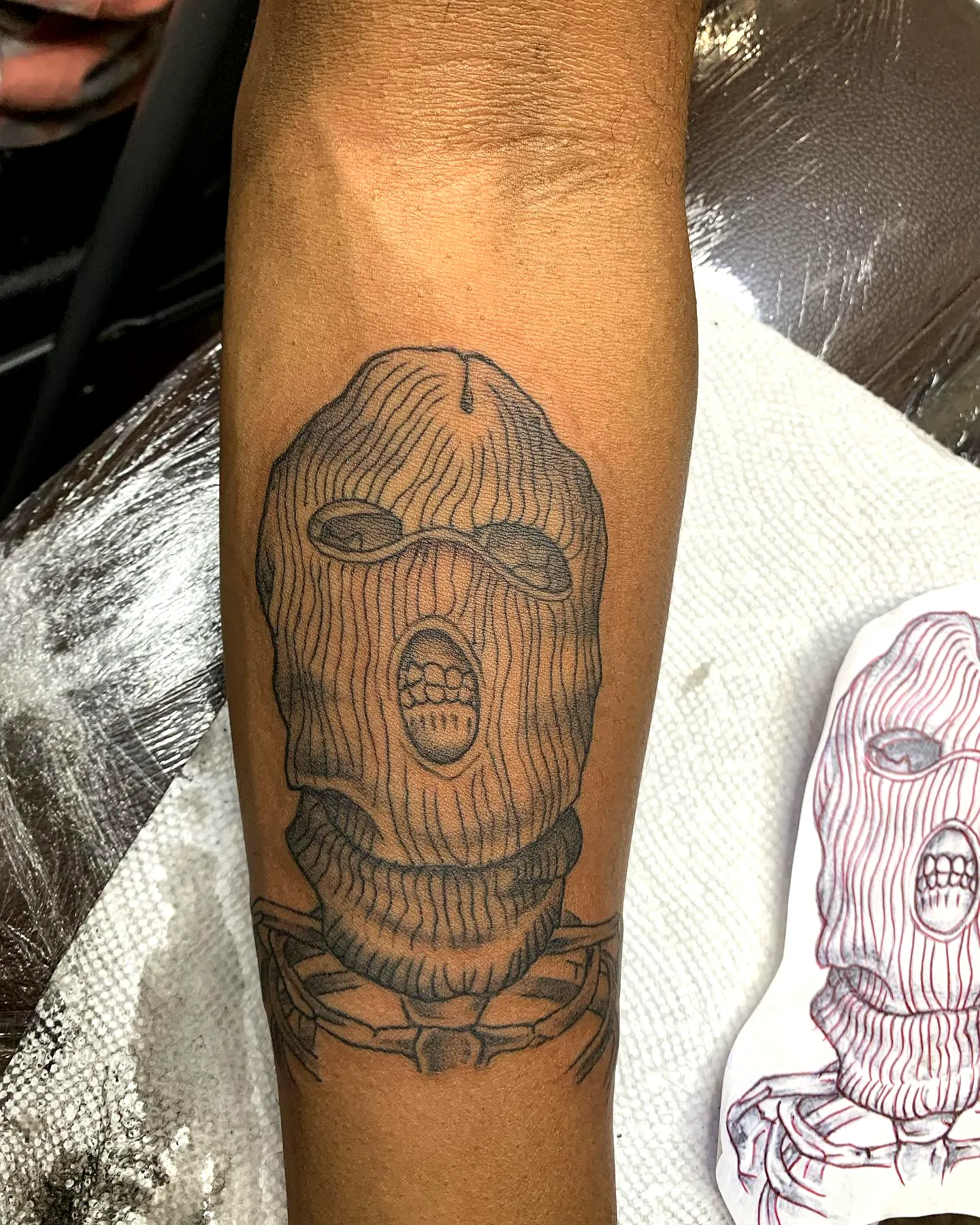 Stylized Hood Forearm Tattoo in Black Ink